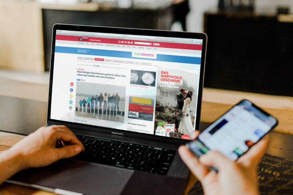 Eine Person hat auf ihrem Laptop einen Artikel auf FOCUS Online aufgerufen. In der rechten Hand hält sie ein Smartphone.
