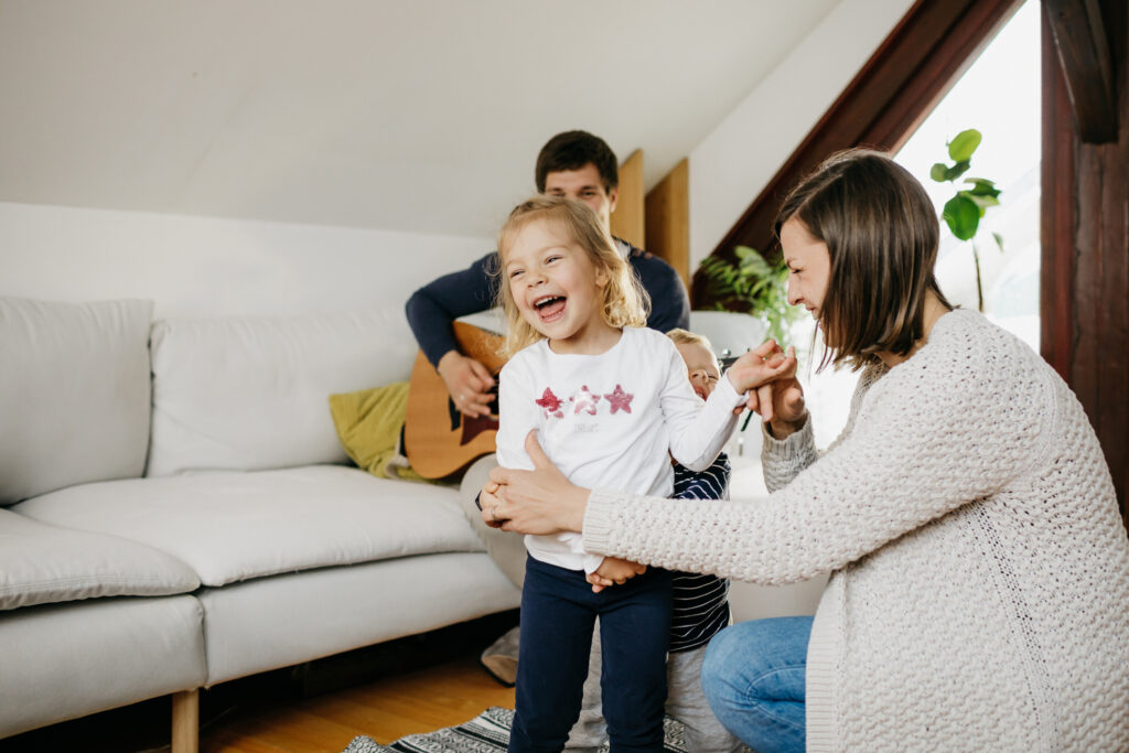 Eine Mutter tanzt mit ihrer Tochter, im Hintergrund spielt der Vater Musik.