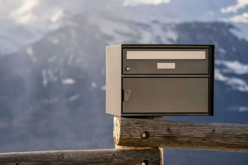 Ein Briefkasten steht auf einem Zaun vor einer Bergkulisse.