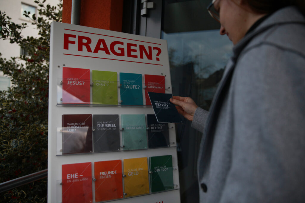 Person greift Flyer aus dem Gemeindeaufsteller