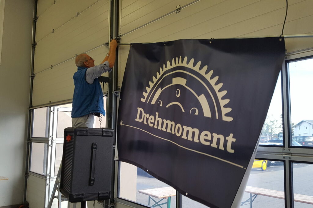 Mann hängt in Werkstattein "Drehmomente"-Banner auf